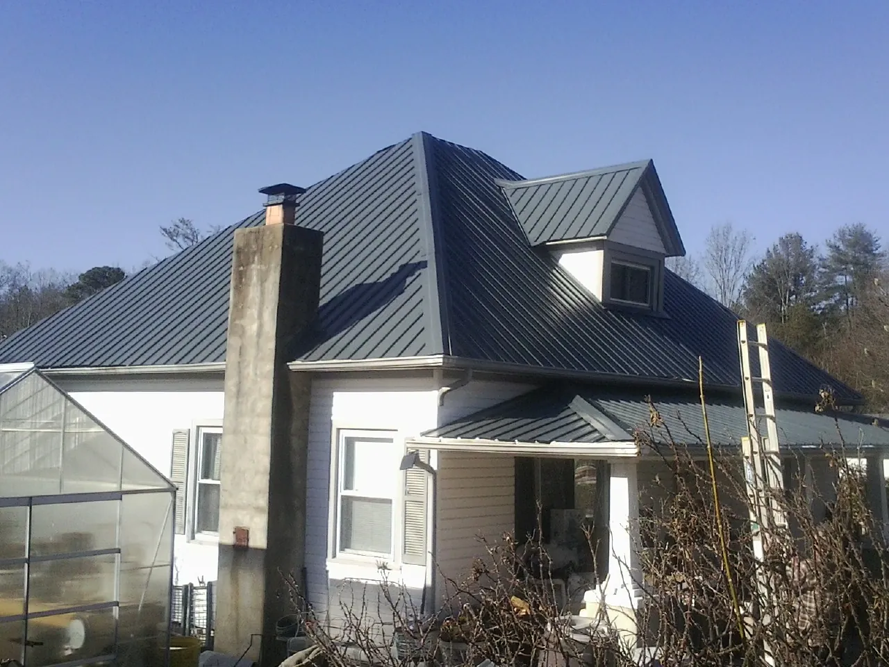 Dark blue standing seam metal roof on a white farmhouse with dormer — Slate & Tile Roof Repair by Roofing Brothers in Ottine