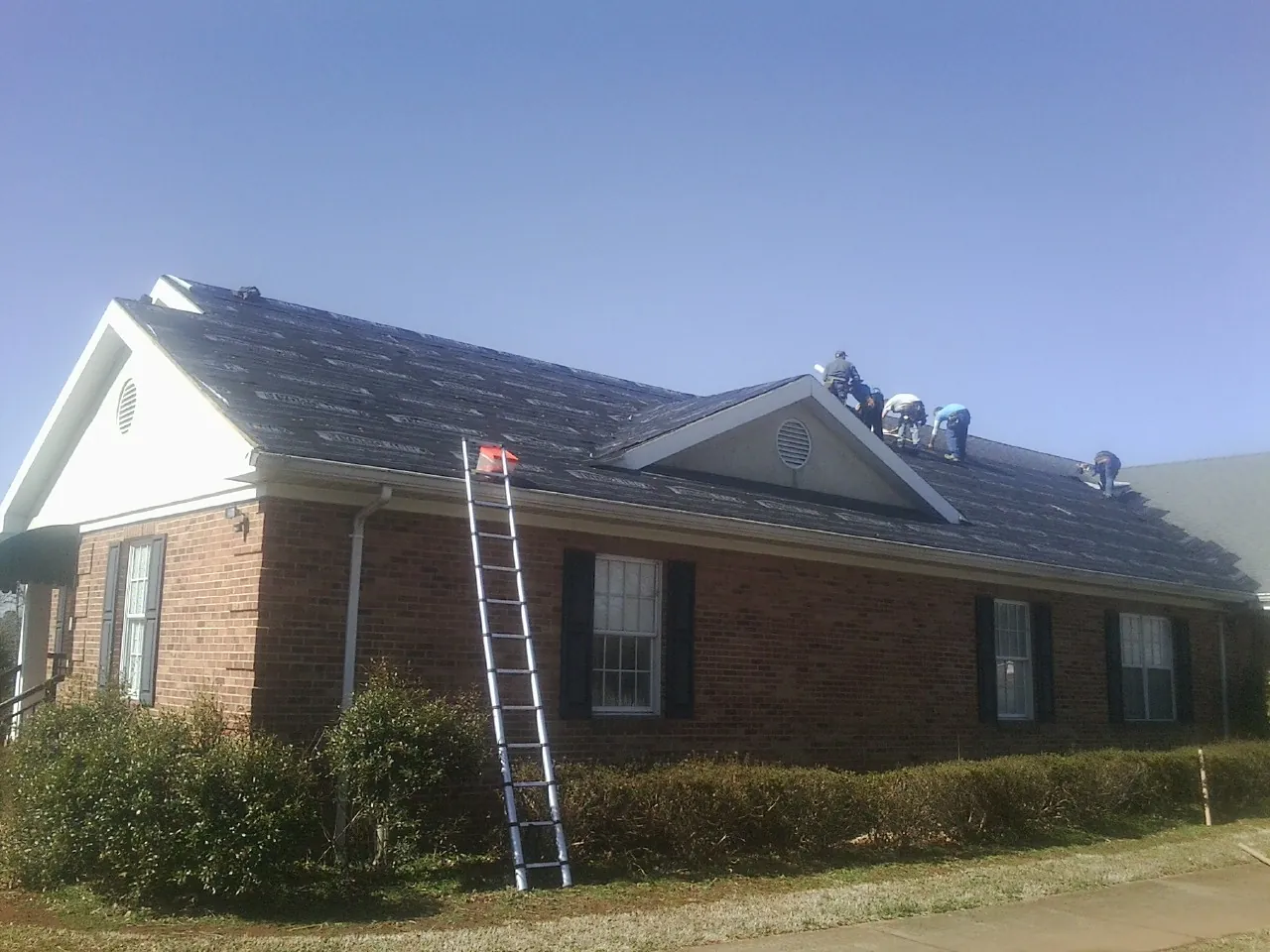 Crew tearing shingles off a brick ranch roof with a ladder set — Metal Roof Repair work by our crew in Ottine