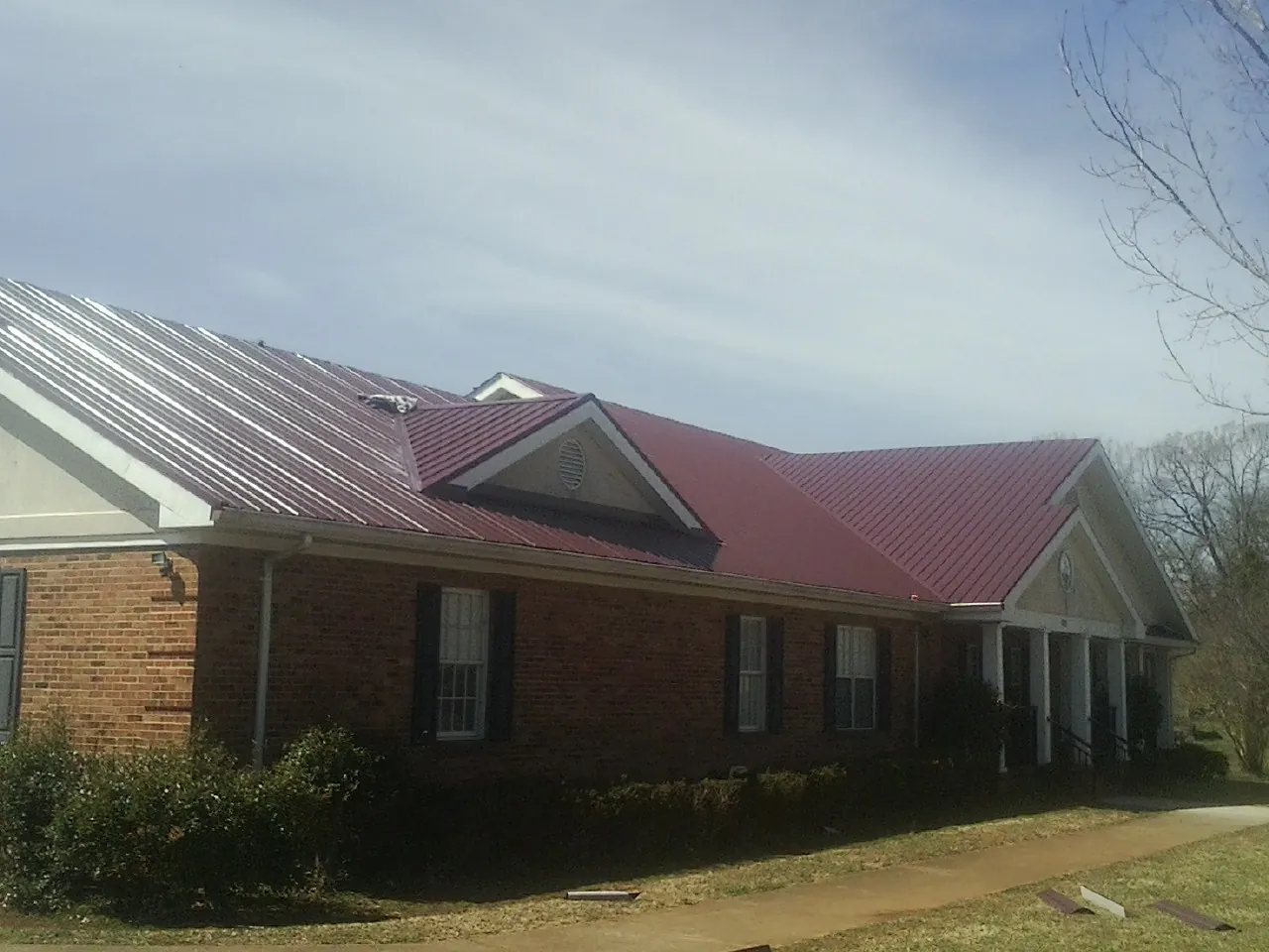 Red metal roof with gabled entries on a long brick building, from a Hail Damage Roof Repair job in Ottine