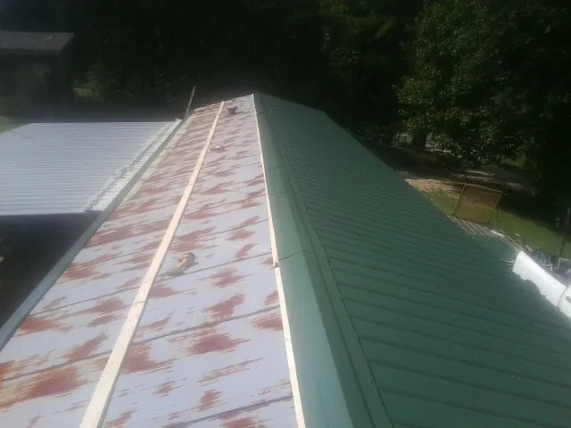 Old rusted panels beside newly installed green metal roofing — Wind Damage Roof Repair by Roofing Brothers in Ottine