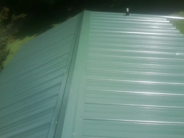 New green metal panels meeting at the ridge of a roof — Flat Roof Repair work by our crew in Ottine