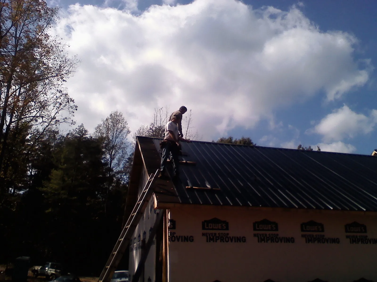Roofer fastening dark metal panels high against a cloudy sky, from a Roof Inspection job in Ottine