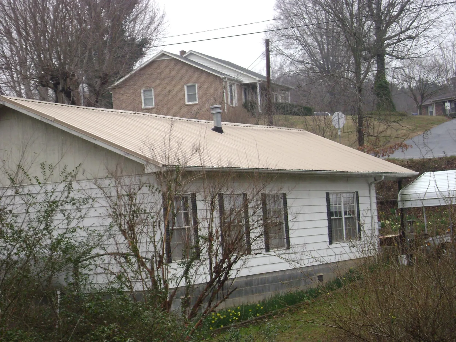 Tan metal roof on a white sided house set into a hillside — Commercial Roofing by Roofing Brothers in Ottine